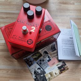 Červený kytarový efekt s třemi černými oválnými knoflíky. Na horní straně je nápis BIG MUFF a bílá číslice 2, níže se nachází logo electro-harmonix s…