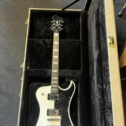 Bílá elektrická kytara s černým pickguardem v otevřeném kufru s černou vnitřní výstelkou. Na hlavě hmatníku je viditelné logo "Epiphone". Nástroj má…