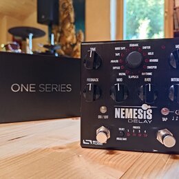 Černý efekt pedál s nápisem NEMESIS DELAY a logem Source Audio v levém dolním rohu. Zařízení má osm ovládacích knoflíků, dva stomečové spínače a červ…