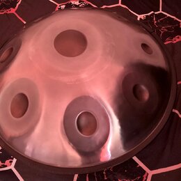 Kupolovitý kovový nástroj typu steel tongue drum v stříbrné barvě. Povrch je lesklý a obsahuje několik kruhových výřezů různých velikostí. Nástroj je…