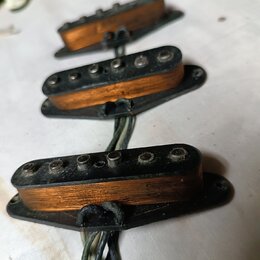 Tři elektrické snímače typu single-coil s oranžovými cívkami a černými plastovými základnami. Snímače mají kovové pólové šrouby a jsou připojeny k če…
