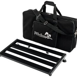 Černý pedalboard s kovovým rámem a pěti protiskluzovými pásy. Vedle něj je černá transportní taška s ramenním popružem a madly. Na přední kapse tašky…