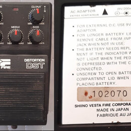 Černý efekt pedál s nápisy VESTA FIRE, DISTORTION a DST. Na horní části jsou čtyři ovládací knoflíky s popisky DISTORTION, TREBLE, MIDDLE a BASS. Dru…