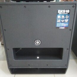 Černý aktivní subwoofer s matným povrchem. V pravém horním rohu je nalepený štítek s nápisy DXS18, 18" Powered Subwoofer a DSP. Uprostřed přední stra…