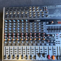 Míchací pult značky behringer, model XENYX X1822USB. Zařízení je v kovovém šasi s množstvím regulačních knoflíků, posuvníků a konektorů. Na horní čás…