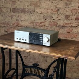 Stříbrný audio zesilovač s černým středovým panelem, umístěný na dřevěném stole. Na levé straně je nápis PIONEER a vedle něj text STEREO INTEGRATED A…
