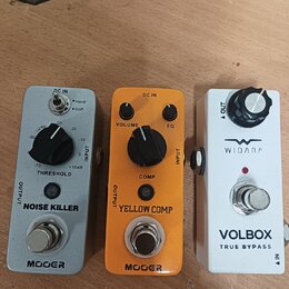 Tři efektové pedály v řadě na dřevěném povrchu. První je šedý s nápisy MOOER, NOISE KILLER a THRESHOLD. Prostřední je oranžový s nápisy MOOER, YELLOW…