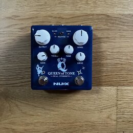 Modrý kytarový efekt s bílými ovládacími knoflíky. Na zařízení jsou nápisy SILVER, SHINE, ROUTING, OUTPUT, TREBLE, TONE, LEVEL, GAIN a DRIVE. Ve spod…