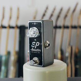 Kompaktní kytarový efekt pedál stříbrné barvy s kovovým šasi. Na čelní straně je nápis „EP“, pod ním slovo „-booster“ a dále text „BY xotic USA“. Ped…