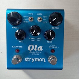 Modrý efekt pedál s nápisy Ola, dBucket Chorus & Vibrato a logem strymon. Na horní straně jsou tři černé otočné knoflíky s popisky SPEED, MIX a DEPTH…