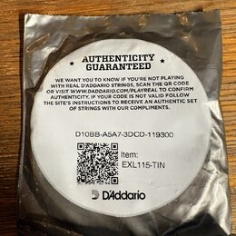 Kruhová bílá nálepka s černým textem umístěná na stříbrném obalu. Na nálepce je nápis AUTHENTICITY GUARANTEED, text s instrukcemi k ověření pravosti…