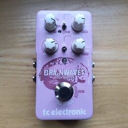 Světle fialový efekt pedál s nápisy BRAINWAVES PITCH SHIFTER a tc electronic. Na horní části jsou čtyři bílé otočné ovladače s popisky FX TYPE, VOICE…