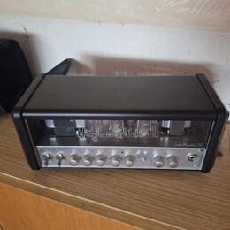 Černý kytarový zesilovač s kovovým předním panelem a průhledným krytem nad elektrony. Na průhledném krytu je bílý nápis „Hughes & Kettner“ a vpravo n…