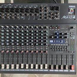 Černý mixovací pult s bílými a červenými popisky. V pravém horním rohu je logo YAMAHA, nápis AUDIO BY Reach a modelové označení Mx12/4 MIXING CONSOLE…