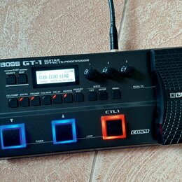 Černý kytarový procesor s nápisem BOSS GT-1 GUITAR EFFECTS PROCESSOR. Zařízení má digitální displej, na kterém je text TERA ECHO LEAD a další ovládac…