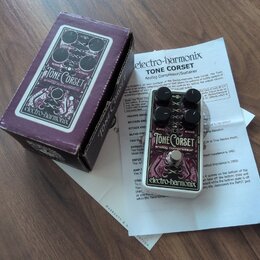 Na fotografii je efekt pedál Electro-Harmonix Tone Corset v bílém provedení s černými ovládacími prvky. Na pedálu jsou nápisy TONE Corset, analog com…