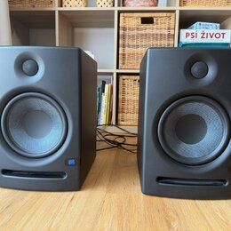 Dva černé studiové monitory v plastovém provedení. Na pravém dolním rohu každého reproduktoru je modrý čtvercový štítek s bílým nápisem JBL. Povrch j…