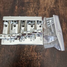 Stříbrný kovový kobylník na elektrickou kytaru s pěti sedly a odpružineným mechanismem. Na horní hraně je vyryt nápis GOTOH JAPAN. Vedle nástroje se…