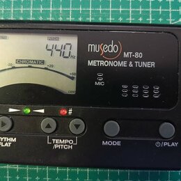 Černý digitální metronom a ladička s LCD displejem. Na přístroji je bílý nápis musedo MT-80 METRONOME & TUNER a označení MIC. Displej zobrazuje hodno…