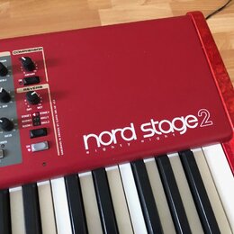 Červený digitální klavír s bílými a černými klávesami. Na horním panelu je bílý nápis nord stage 2 a pod ním menší text eighty eight. V levé části js…