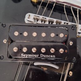 Černý humbucker s dvěma řadami snímacích pólů, umístěný v černém plastovém rámečku na černé kytare. Na spodní části snímače je bílý nápis Seymour Dun…