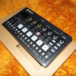 Černý kompaktní sampler Roland SP-S s numerickou klávesou od 1 do 6 a řadou ovládacích tlačítek. Na horní části je logo Roland a označení SP-S, dále…