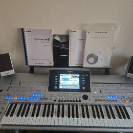 Stříbrný digitální klavír s nápisem YAMAHA a označením Tyros 4. Nástroj má v centru barevný displej, zahlreiche ovládací tlačítka a modře podsvícené…