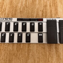 Stříbrný MIDI pedál s černými spínači a dvěma expresními pedály. Na levé straně je nápis FCB1010 MIDI FOOT CONTROLLER a nad spínači jsou sekce PRESET…