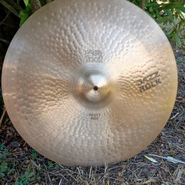 Kovový činel s kladivkovaným povrchem a zlatavou barvou. Na povrchu jsou vyraženy nápisy „paiste 2002“, „JAZZ ROCK“ a „HEAVY RIDE“. Povrch vykazuje d…