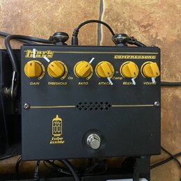 Černý efekt pedál s nápisy Markbass a COMPRESSORE. Na horní části jsou šest žlutých otočných ovladačů s popisky GAIN, THRESHOLD, RATIO, ATTACK, RELEA…