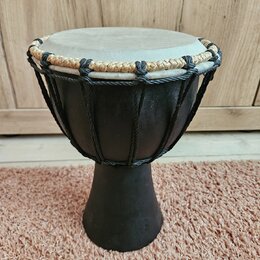 Černý djembe s hrací plochou z pleti v přirozené světlé barvě. Horní okraj je opleten kombinací černého a béžového provázku. Na těle nástroje nejsou…