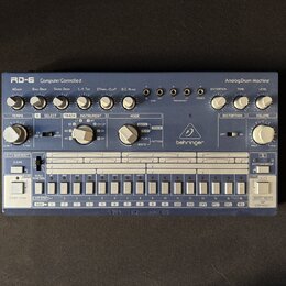 Modré analogové bicí automaty s bílými popisky a ovládacími prvky. Na přístroji jsou nápisy RD-6 Computer Controlled Analog Drum Machine a logo behri…