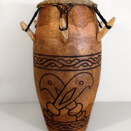 Dřevěný buben s hnědým povrchem a koženou membránou, která je upevněna černými provazy. Tělo nástroje obsahuje vyřezávané ornamenty ve formě vlnitých…