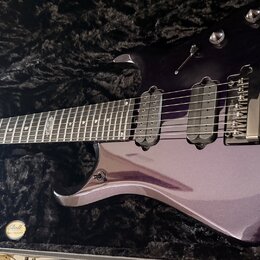 Fialová elektrická kytara v černém polstrovaném kufru. Na hmatníku je viditelný nápis "Custom Shop". Kytara má dva snímače typu humbucker a fixní mos…