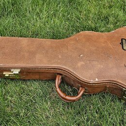 Hnědý tvrdý kufýr na kytaru s kovými zapínacími zámky a úchytem. Na pravé straně je vidět černé logo s nápisy USA a Gibson. Povrch vykazuje známky op…
