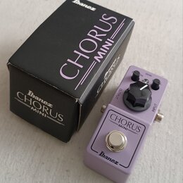Fialový efekt pedál s nápisy CHORUS MINI a Ibanez. Na horní části je jeden černý ovládací knoflík a konektory OUTPUT a INPUT. Vedle pedálu je černá k…