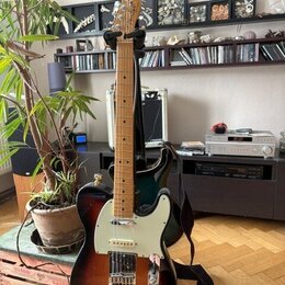 Elektrická kytara s tmelelovým povrchem v přechodu od černé k hnědé a žluté barvě. Na hlavě je viditelné logo Fender. Kytara má bílý pickguard, jeden…