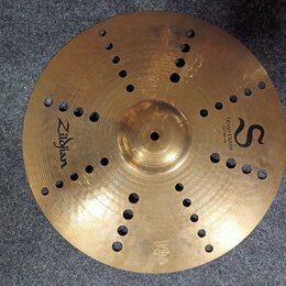Zlatý kovový činel s otvory v povrchu. Na povrchu jsou nápisy Zildjian, TRASH CRASH a 16"/40 cm spolu s logem ve tvaru písmene S. V dolní části je dr…