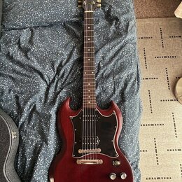 Elektrická kytara s červeně hnědým lakem a černým pickguardem. Na hlavě krku je viditelné logo Epiphone. Nástroj vykazuje mírné opotřebení povrchu v…