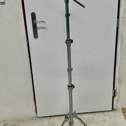 Stříbrný kovový mikrofonní stojan s trojnožkou a teleskopickým stoupacím mechanismem. Horní část obsahuje kloubový ramene s držákem na mikrofon. Na s…