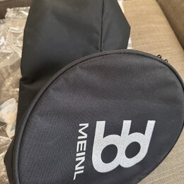Černý textilní obal oválného tvaru s bílým logem a nápisem MEINL. Vedle něj je umístěn další černý textilní obal. Povrch materiálů vypadá čistě a v d…