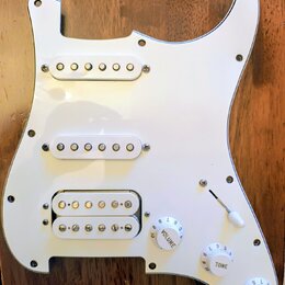 Bílá pickguard pro elektrickou kytaru s třemi snímači. Horní dva snímače jsou jednoduché (single-coil) a spodní je humbucker s dvěmi řadami pólů. Sou…