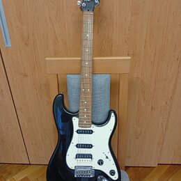 Černá elektrická kytara s bílým pickguardem a hnedým hmatníkem. Na hlavě je viditelné logo Squier. Nástroj má tři snímače typu single-coil a chromova…