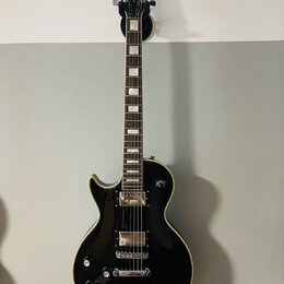 Černá elektrická kytara s tvarem singlecut a krémovým lemováním. Na hlavě je bílý nápis Bach. Nástroj má dva humbuckery, čtyři ovládací knofíky a stр…