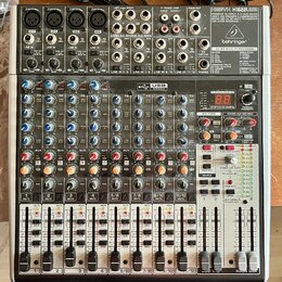 Stříbro-šedý mixážní pult s černými ovládacími prvky. V pravém horním rohu je nápis XENYX X1622USB a logo behringer. Přístroj obsahuje více vstupních…