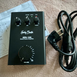 Černý kompaktní zesilovač s nápisy Harley Benton, GPA-100 a Guitar Power Amplifier. Na horní straně jsou tři ovládací knoflíky s popisky BASS, MID a…