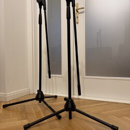 Dvě černé mikrofonní stativy s trojnožkou z kovového materiálu. Na jedné z nožek pravého stativu je viditelné kulaté logo s nápisem Gravity. Povrch s…