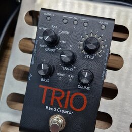 Černý efekt pedál s nápisem TRIO Band Creator. Zařízení obsahuje několik ovládacích prvků: otočný přepínač GENRE s označením ALT ROCK, ROCK, COUNTRY,…