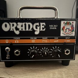Černý kytarový zesilovač s kovovou rukojetí a oranžovým pruhem na předním panelu. Na horní části je bílý nápis ORANGE a vedle něj text MICRO DARK, v…