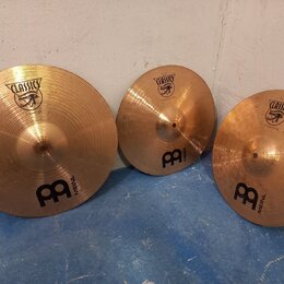 Tři mosazné činely různých velikostí opřené o bílou zeď. Každý činel má nápis CLASSICS v logu s motivem ptáka a logo MEINL. Povrch činelů je jemně br…